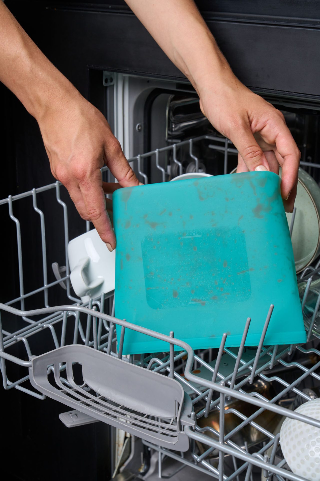 Eine Person stellt einen benutzten, wiederverwendbaren türkisen Toppits Silikonbeutel in die Spülmaschine 