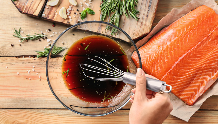 Dunkle Marinade mit Kräutern wird neben frischem Lachsfilet auf Toppits Backpapier angerührt
