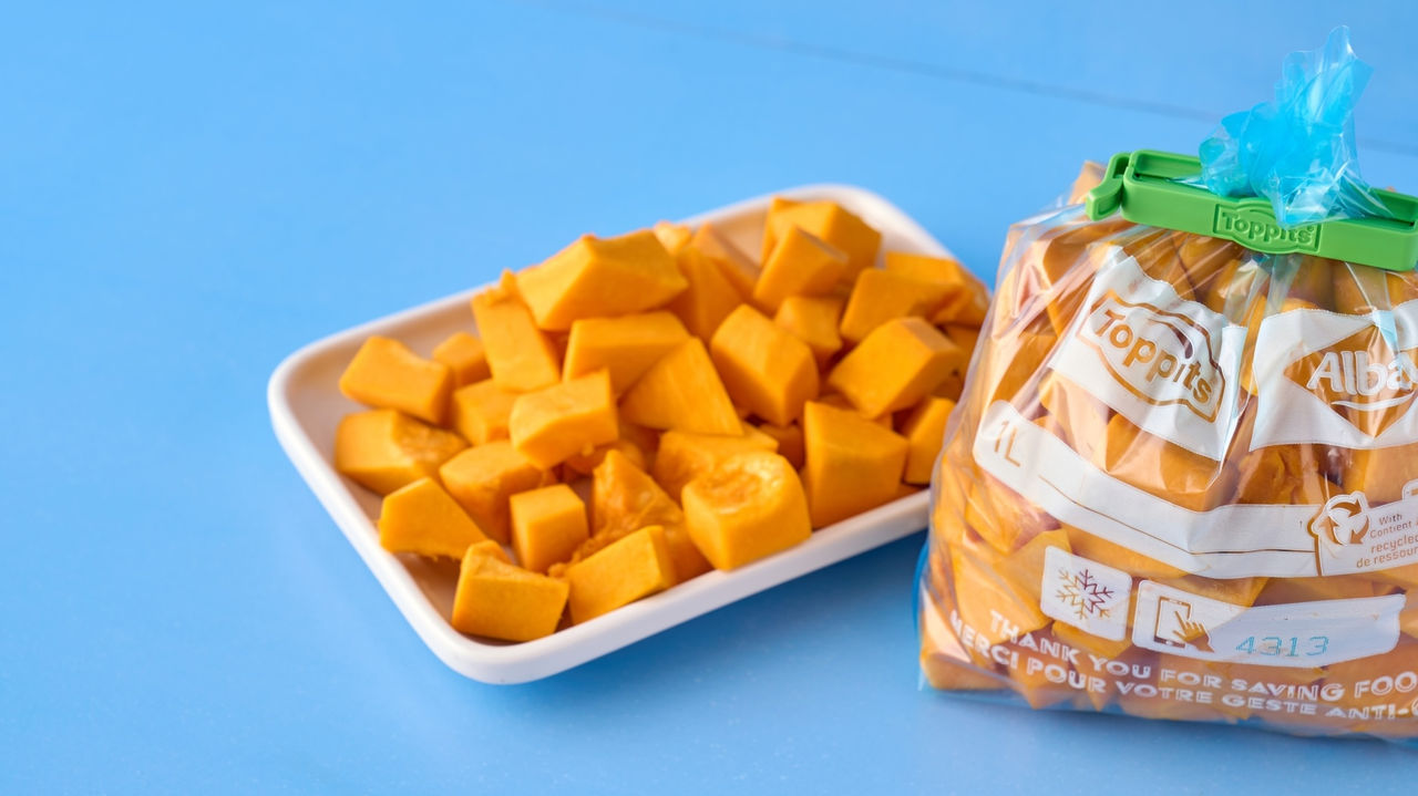 Geschnittener Kürbis in Toppits Beutel mit Clipverschluss neben weißer Schale auf blauem Untergrund.