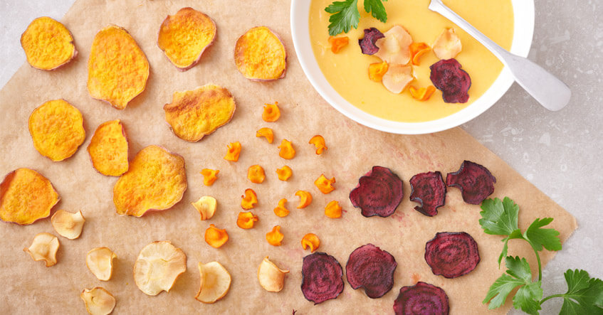 Gemüsechips von Pastinake, Süßkartoffel, Möhre und Rote Bete auf Backpapier, dazu Süßkartoffelsuppe in der Schale