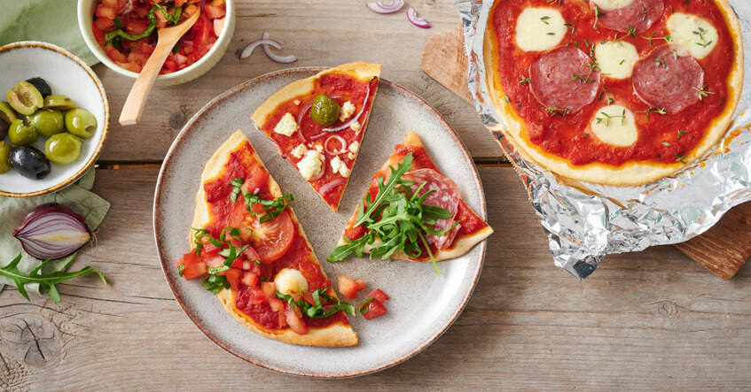 Bunt belegte Pizza auf dem Teller und auf Toppits Alufolie