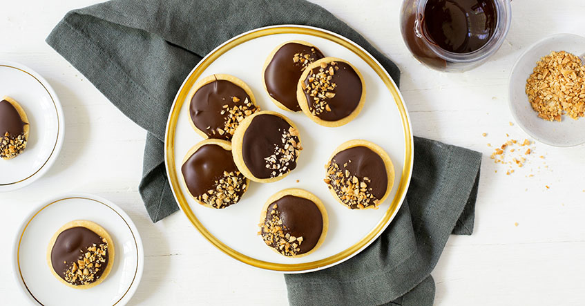 Salted Caramel Cookies auf einem Teller mit Kuvertüre und gehackten Erdnüssen